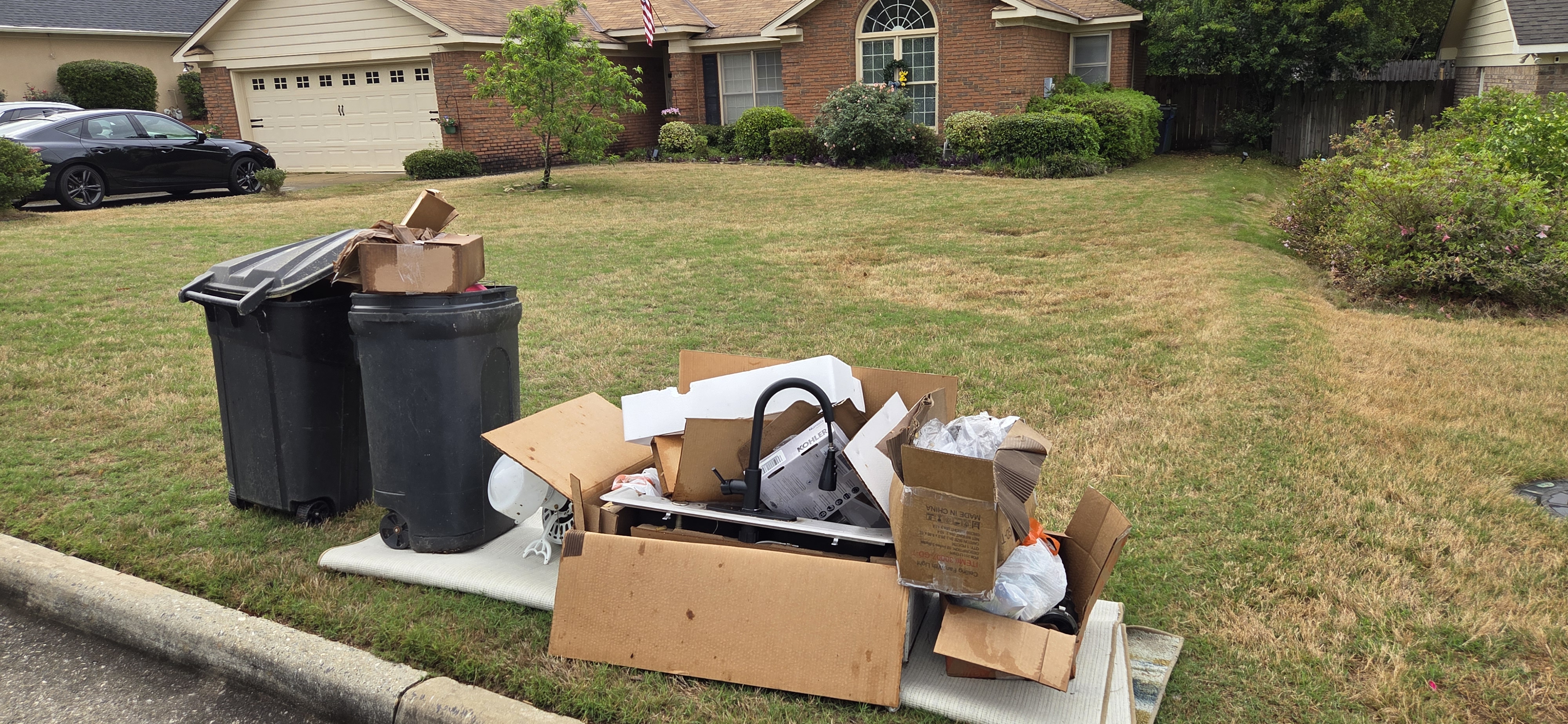 Curbside junk pile with trash cans in Columbus GA — cardboard boxes and mixed bulk items