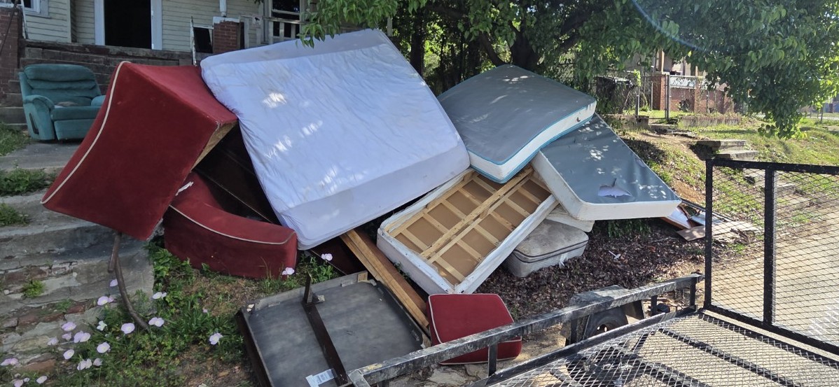 Large pile of furniture and mattresses at a Columbus GA property — sofas, bed frames, and debris