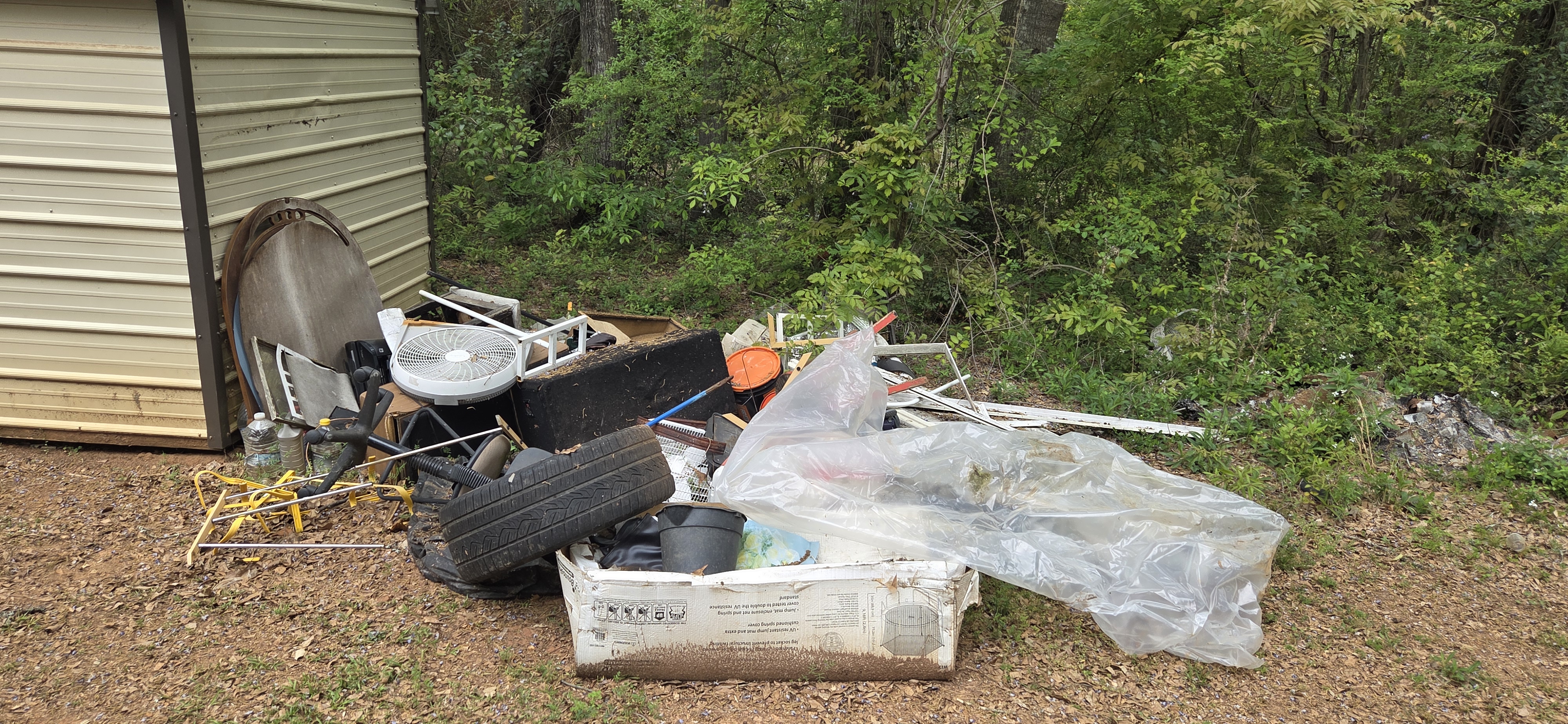 Mixed outdoor junk pile beside shed before haul-off — satellite dish, tires, bags, and debris — Go Forward Haulers